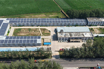 Aerial view of a building with solar panels on its roof, surrounded by green fields and trees.